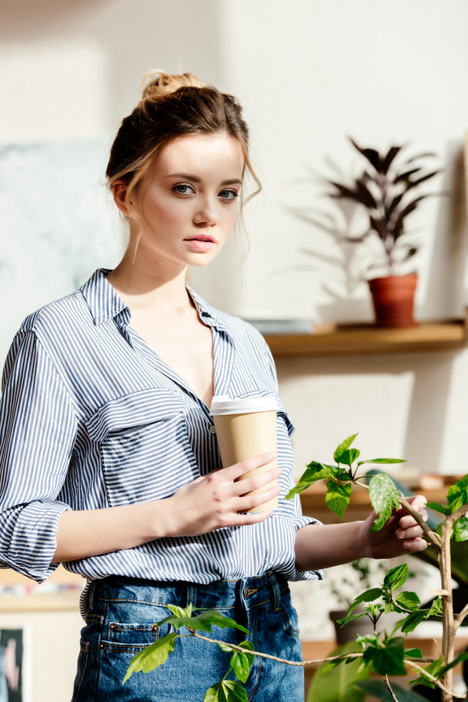 retrato de mujer joven con taza de papel de café tocando maceta planta
  - Foto, Imagen