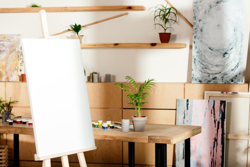 Wnętrze studio artysty ze sztalugami i stół z malarstwa dostaw i roślina doniczkowa  - Zdjęcie, obraz