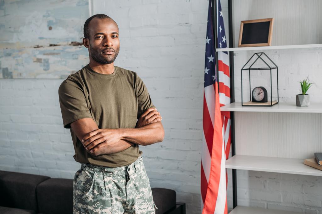 Homme confiant en vêtements de camouflage debout dans la chambre avec drapeau
 - Photo, image
