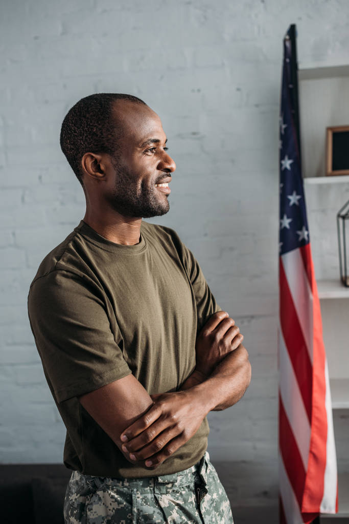 Soldato afroamericano con braccia incrociate in piedi in camera con bandiera
 - Foto, immagini