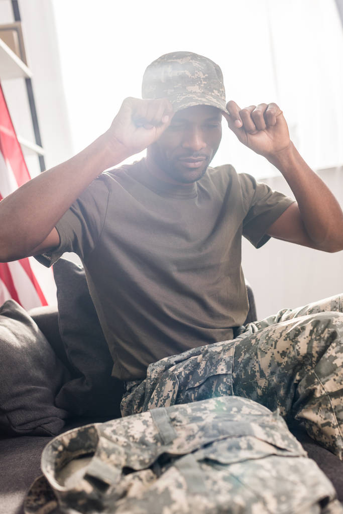 Guapo soldado poniéndose la gorra mientras está sentado en el sofá
 - Foto, imagen