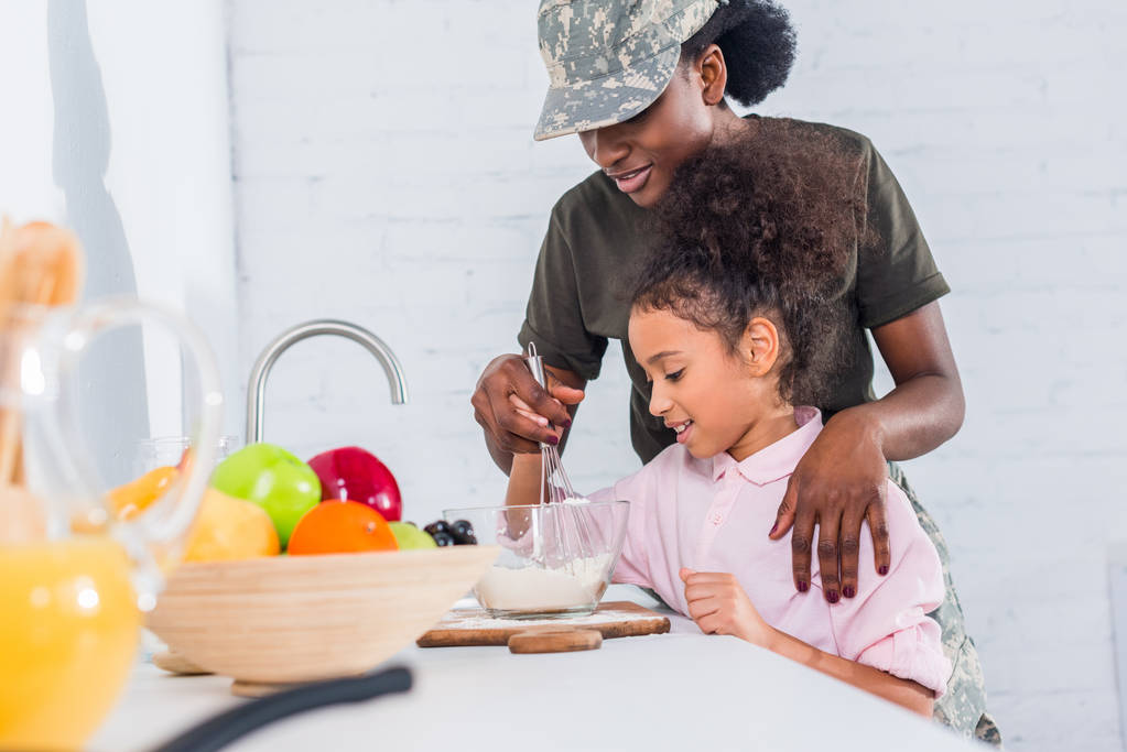 Afro-Amerikaanse soldaat met dochtertje koken samen thuis keuken - Foto, afbeelding