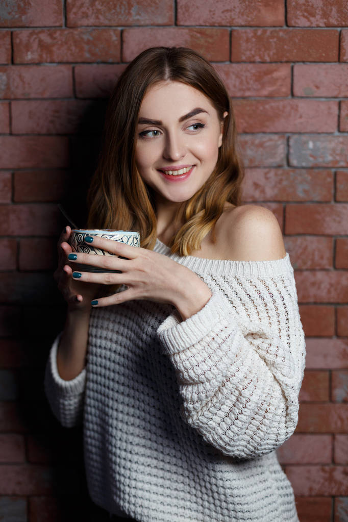 Joven hermosa mujer bebiendo una taza de café en el café sobre un fondo de pared de ladrillo rojo. Elegante dama con bebida caliente
. - Foto, Imagen