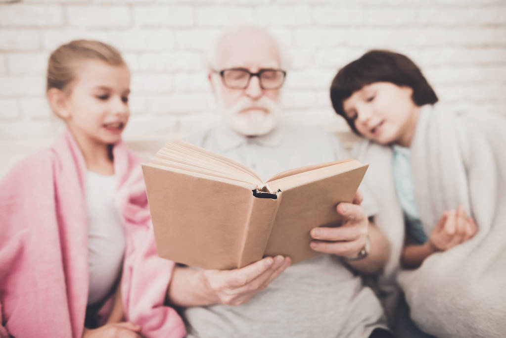 Abuelo leyendo libro con niños en casa
 - Foto, imagen