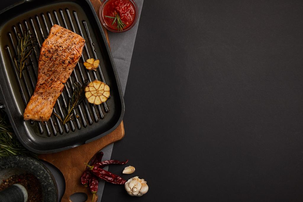 вид сверху на приготовленный на гриле стейк из лосося на деревянной доске, ингредиенты и соус на черном столе
 - Фото, изображение