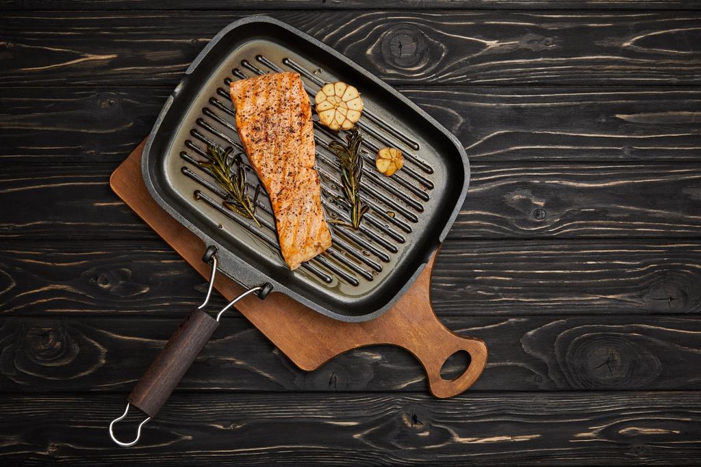 вид сверху на приготовленный на гриле стейк из лосося с розмарином на разделочной доске на черном деревянном столе
 - Фото, изображение