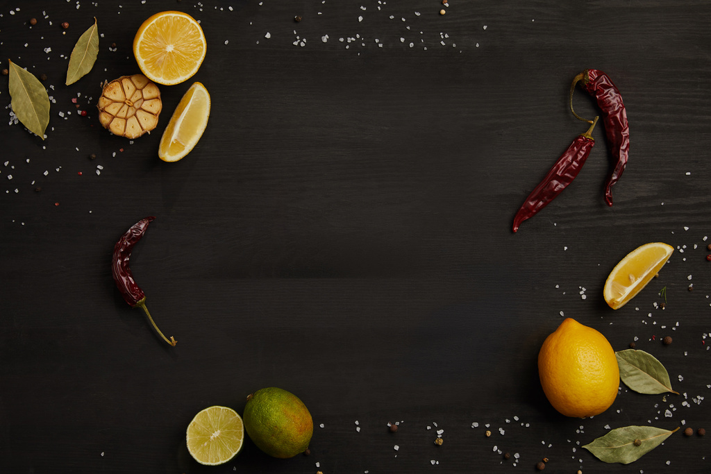 vlakke leggen met citroen en limoen stukken, specerijen, chili pepers en laurierblaadjes op zwart tafelblad - Foto, afbeelding