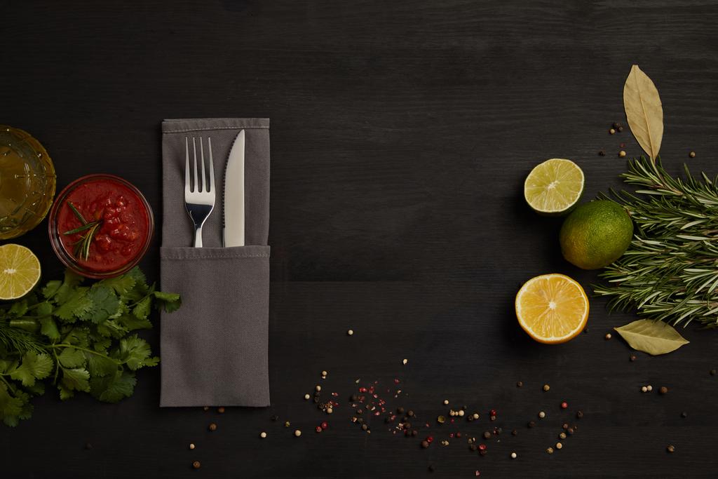 flat lay with cutlery, sauce, rosemary, spices and citrus fruits pieces on black tabletop - Photo, Image