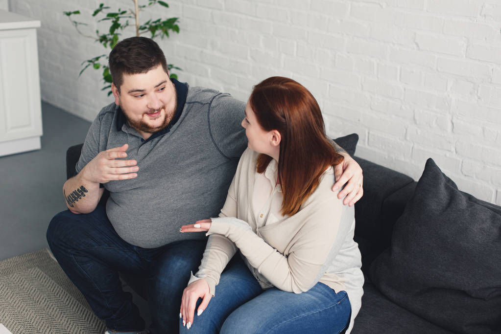 sobrepeso novio y tamaño más novia hablando y haciendo gestos en el sofá en casa
 - Foto, imagen