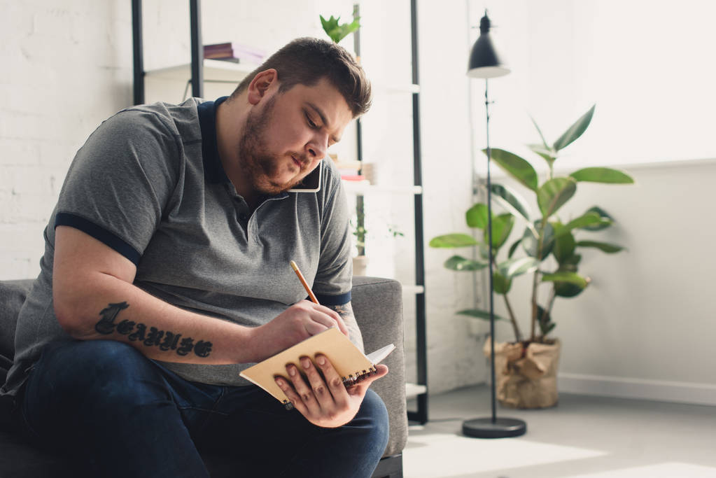 Obézní muž psát něco k notebooku na pohovce doma - Fotografie, Obrázek