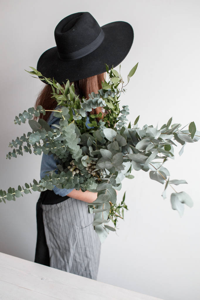 Florist stellt einen Strauß her. Arbeitsprozess. Frau hält einen Strauß Eukalyptus in den Händen - Foto, Bild