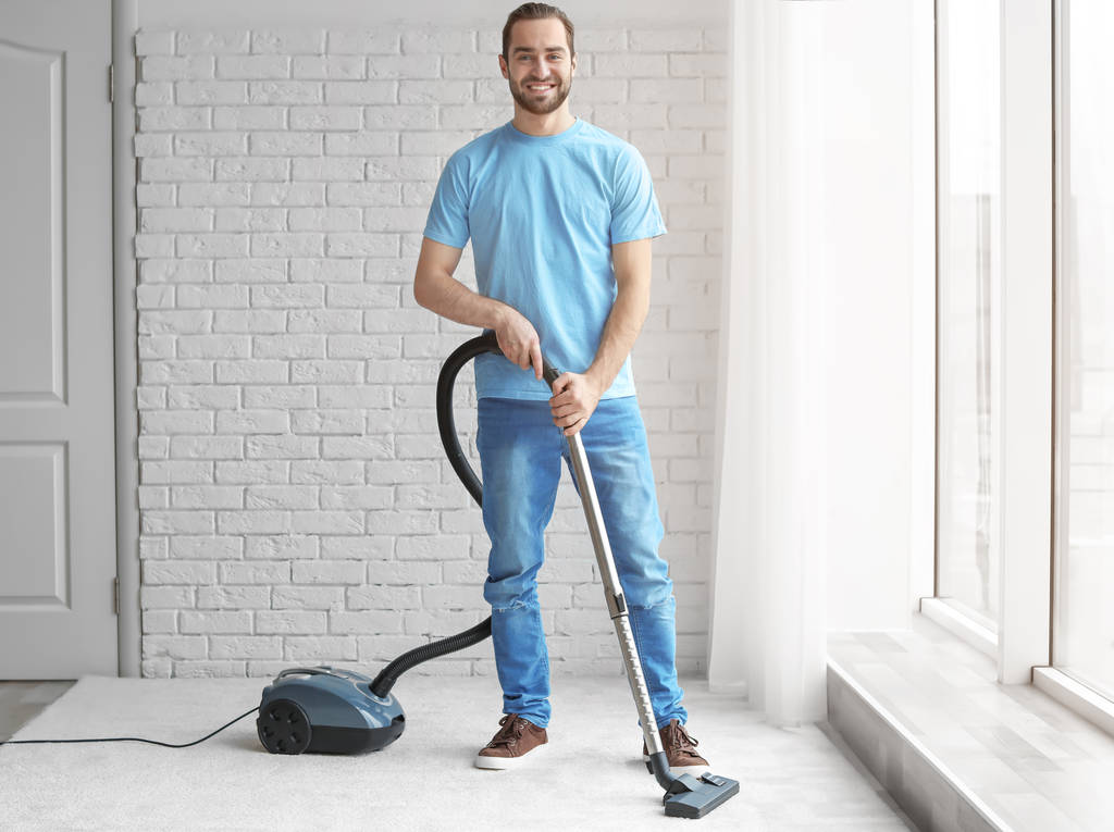 Jeune homme nettoyage tapis avec aspirateur à la maison
 - Photo, image
