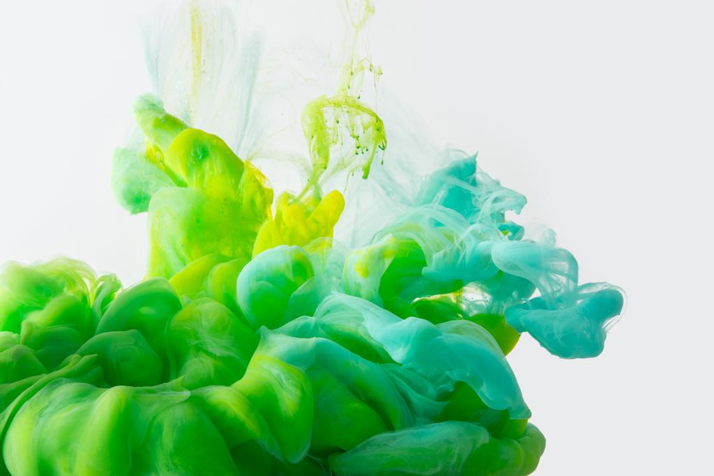 Κλείνω πάνω θέα της ανάμειξης του πράσινου, κίτρινου και φωτεινά γαλαζοπράσινα μελάνια πιτσιλιές στο νερό που απομονώνονται σε γκρι - Φωτογραφία, εικόνα