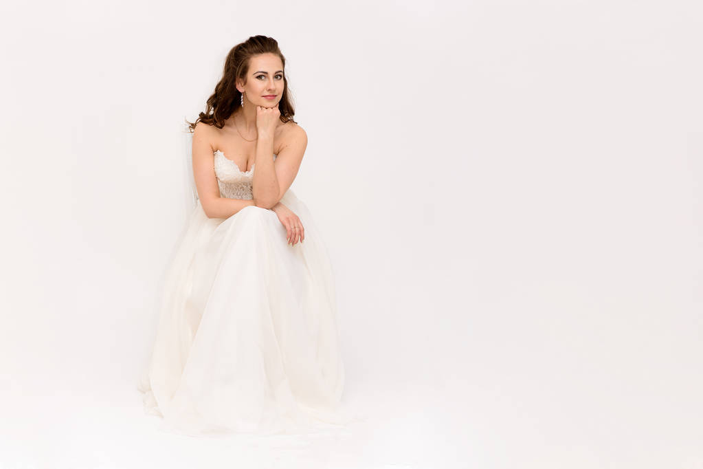 mooie bruid in witte trouwjurk in verschillende poses op een witte achtergrond toont verschillende emoties - Foto, afbeelding