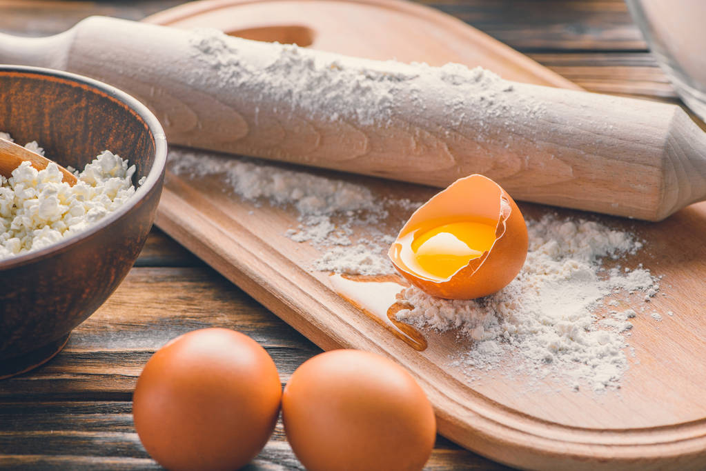 Vista de cerca de huevos crudos, harina con rodillo y requesón sobre mesa de madera
 - Foto, Imagen