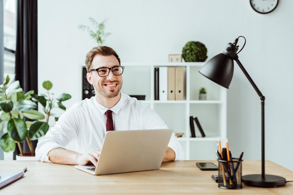 glimlachend zakenman die werken met de laptop op werkplek in moderne kantoren - Foto, afbeelding