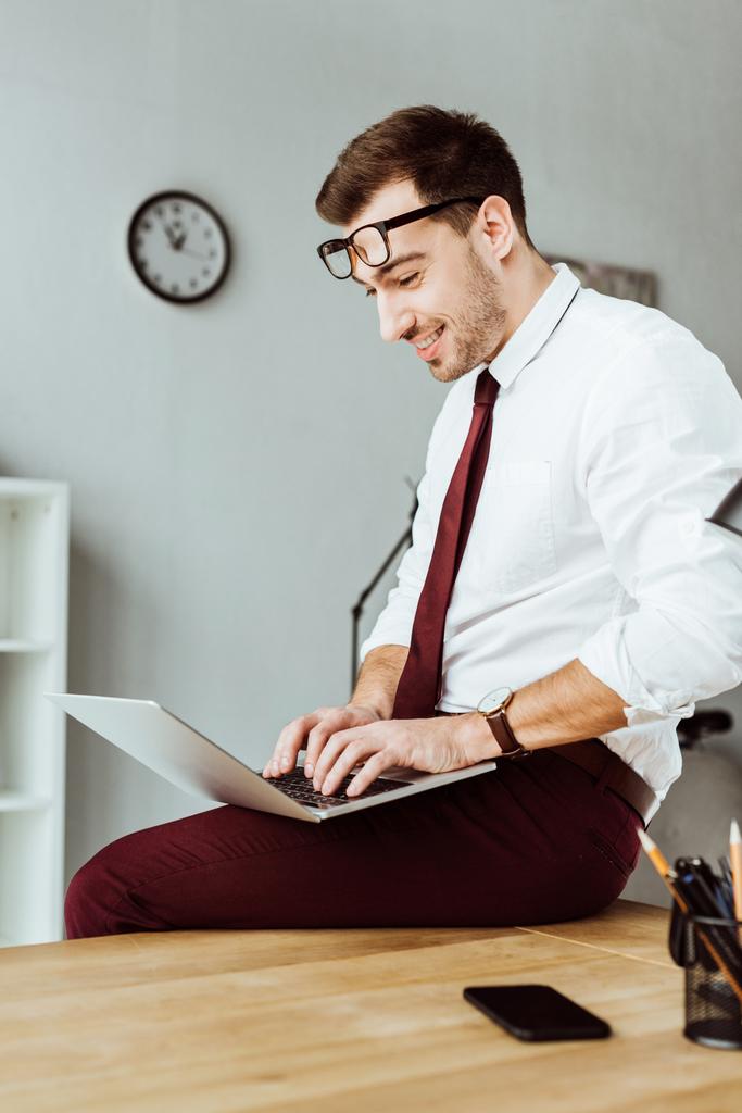 веселий бізнесмен, використовуючи ноутбук, сидячи на столі в офісі
 - Фото, зображення