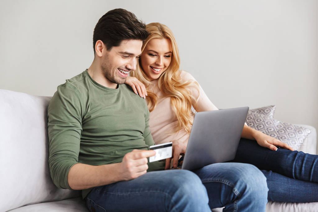 デビット カードを保持しているソファの上に座って幸せな若い夫婦. - 写真・画像