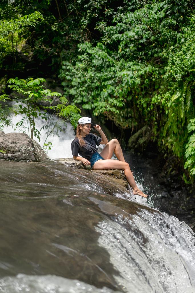 боковой вид женщины в кепке, отдыхающей на скалах возле водопада Алин-Алинь, Бали, Индонезия
 - Фото, изображение