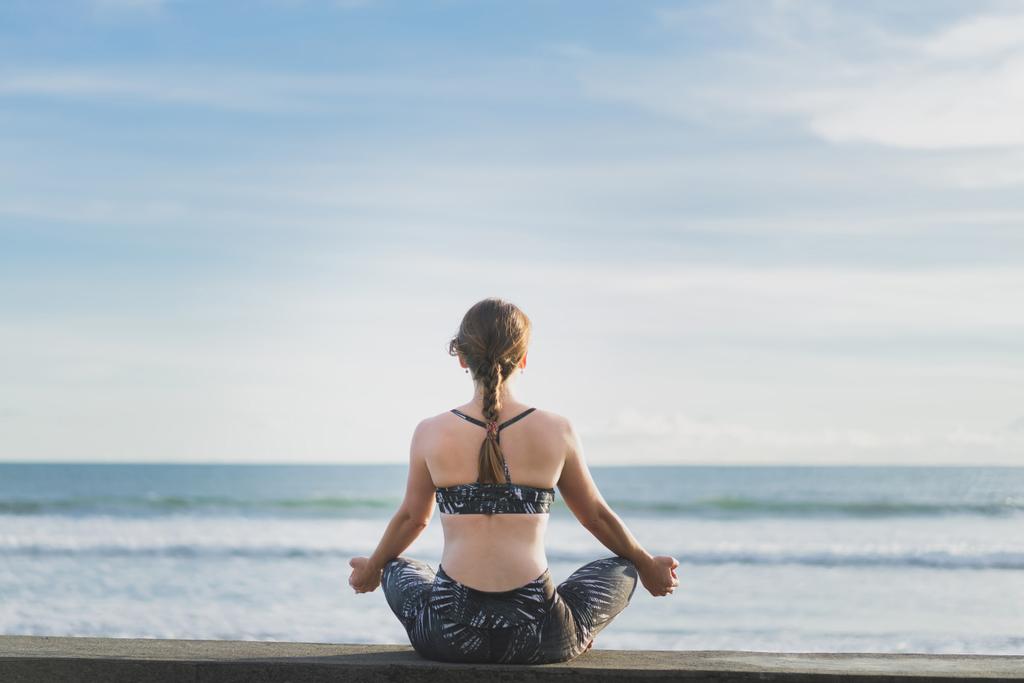 zadní pohled na ženy, meditoval v lotosové pozici s oceánem a modré obloze na pozadí, Bali, Indonésie - Fotografie, Obrázek