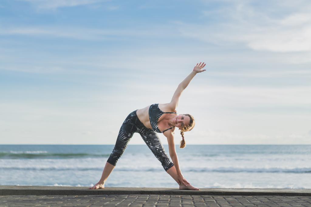 femme pratiquant le yoga en triangle étendu Pose avec l'océan et le ciel bleu sur fond, Bali, Indonésie
 - Photo, image
