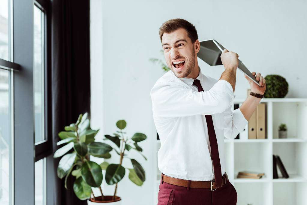 agresivo empresario gritando y lanzando portátil en la oficina moderna
 - Foto, imagen