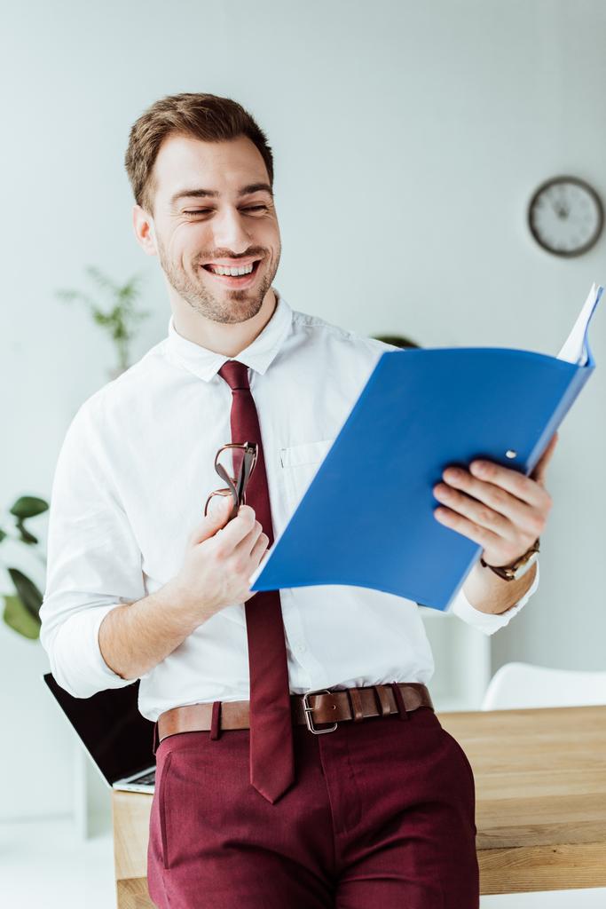handsome smiling businessman looking at folder with documents - Photo, Image