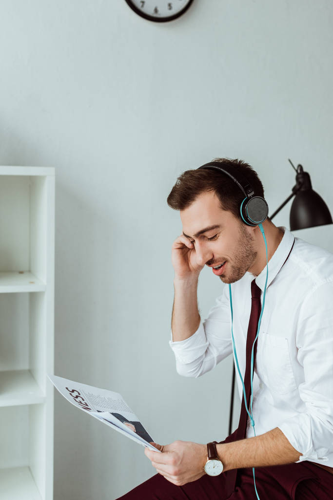νεαρός επιχειρηματίας ακούγοντας μουσική στα ακουστικά και να διαβάζει Εφημερίδα - Φωτογραφία, εικόνα