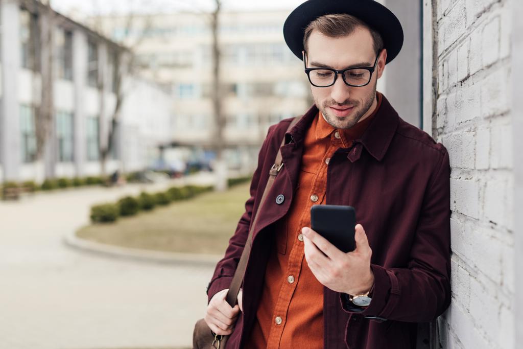 szép stílusos ember használ smartphone Porzsákos divatos ruhák - Fotó, kép