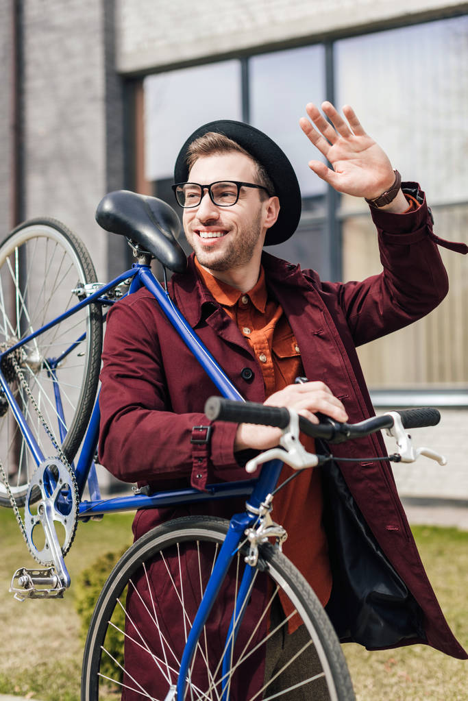 handsome smiling man waving and carrying bicycle   - Photo, Image
