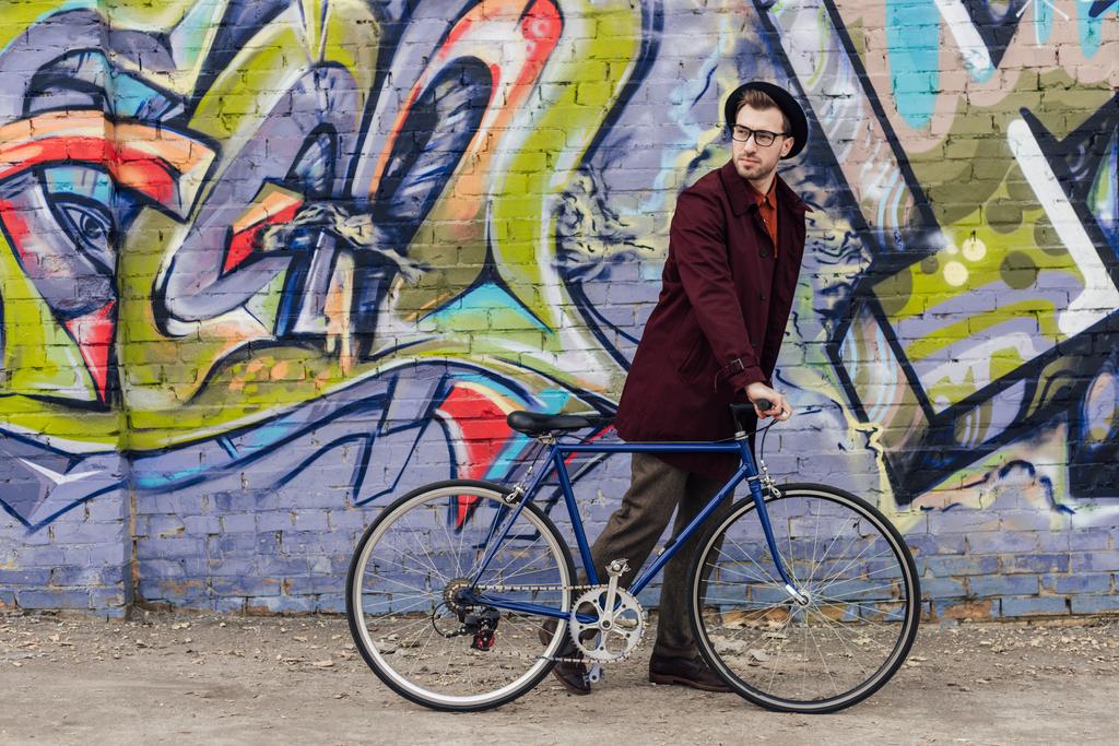 Stylowy elegancki człowiek stojący z roweru w ścianie z graffiti - Zdjęcie, obraz