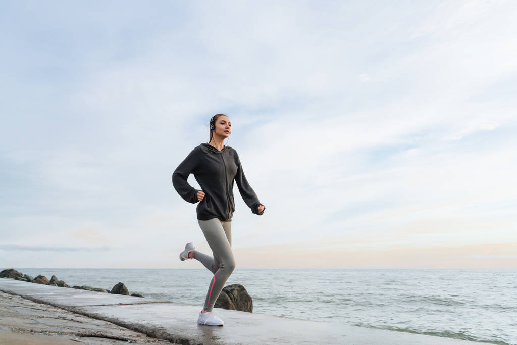 Spor, açık havada, sahil boyunca çalışır bir maraton için hazırlamak için atletik genç kız gider - Fotoğraf, Görsel