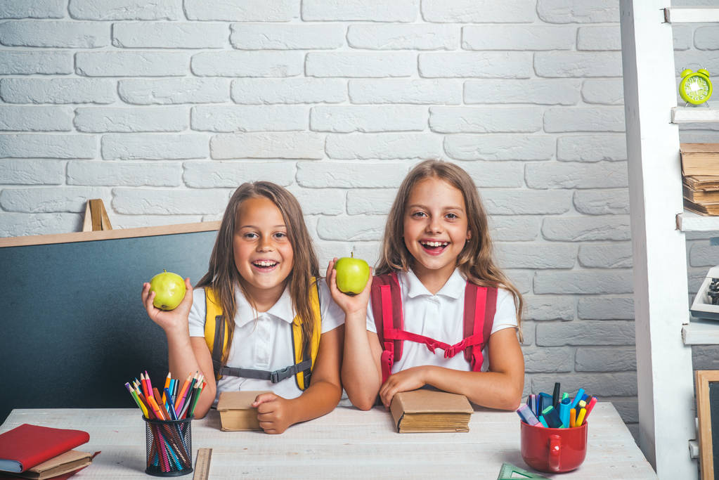 学校、ホーム スクーリングに戻る。知識の日に教室で小さな姉妹の友情。小さな女の子は、昼休みでリンゴを食べる。女の子の学校の時間。9 月 1 日のレッスンで幸せな学校の子供たち - 写真・画像