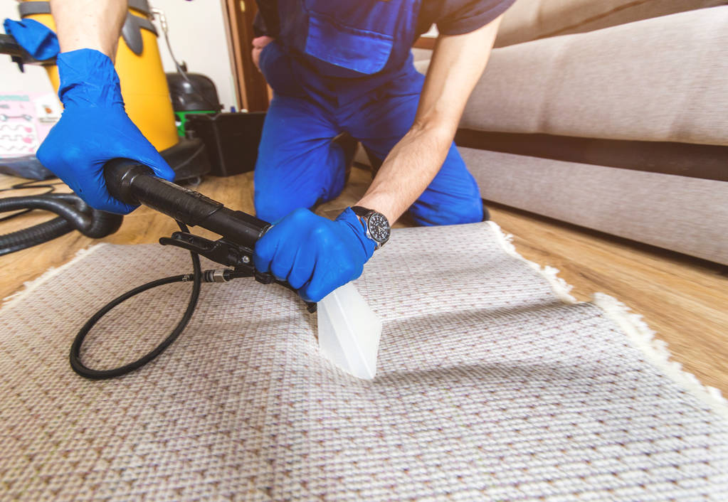 Reinigungsservice. Mann Hausmeister in Handschuhen und Uniform saugen weißen Teppich mit professioneller Ausrüstung - Foto, Bild