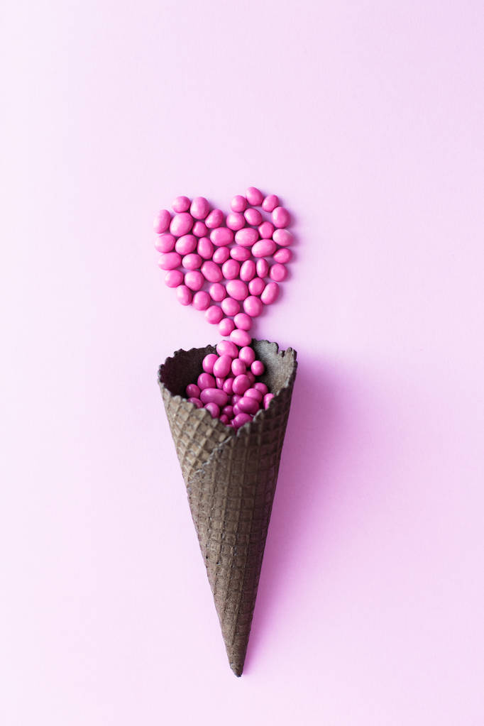 paarse gelei bonen snoep verspreid in de vorm van een hart van een zwarte wafel kegel op een Lila achtergrond - Foto, afbeelding
