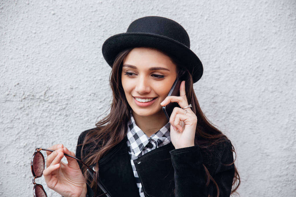 Gülümseyen kentsel kız akıllı telefon Yüzünde gülümsemeyle kullanır. Moda kız açık havada eğleniyor bir rock siyah stil giyen portresi - Fotoğraf, Görsel
