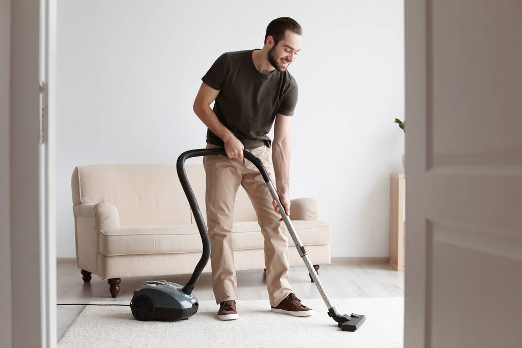 Junger Mann putzt Teppich mit Staubsauger im Wohnzimmer - Foto, Bild