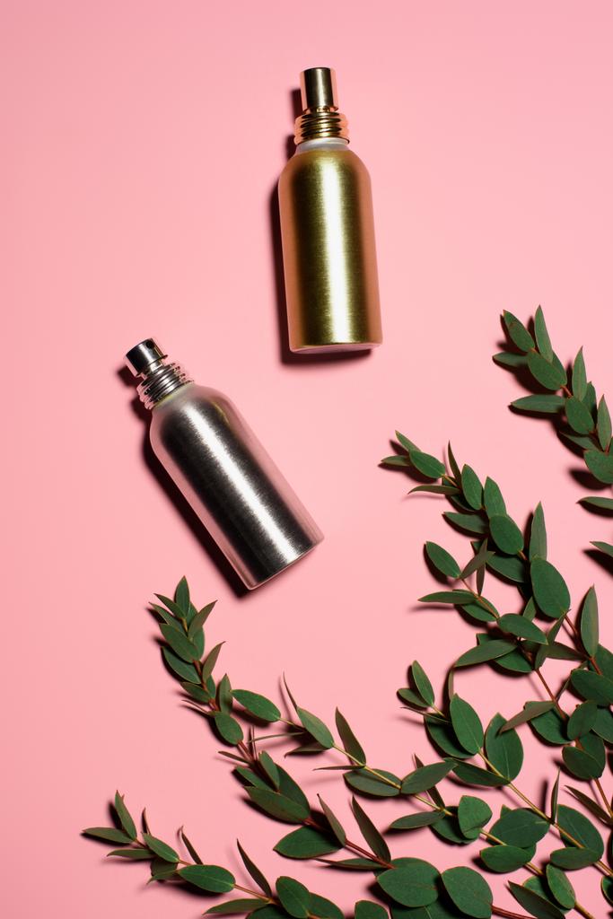 felülnézet fém palack parfümök zöld ágakat, rózsaszín felületen - Fotó, kép