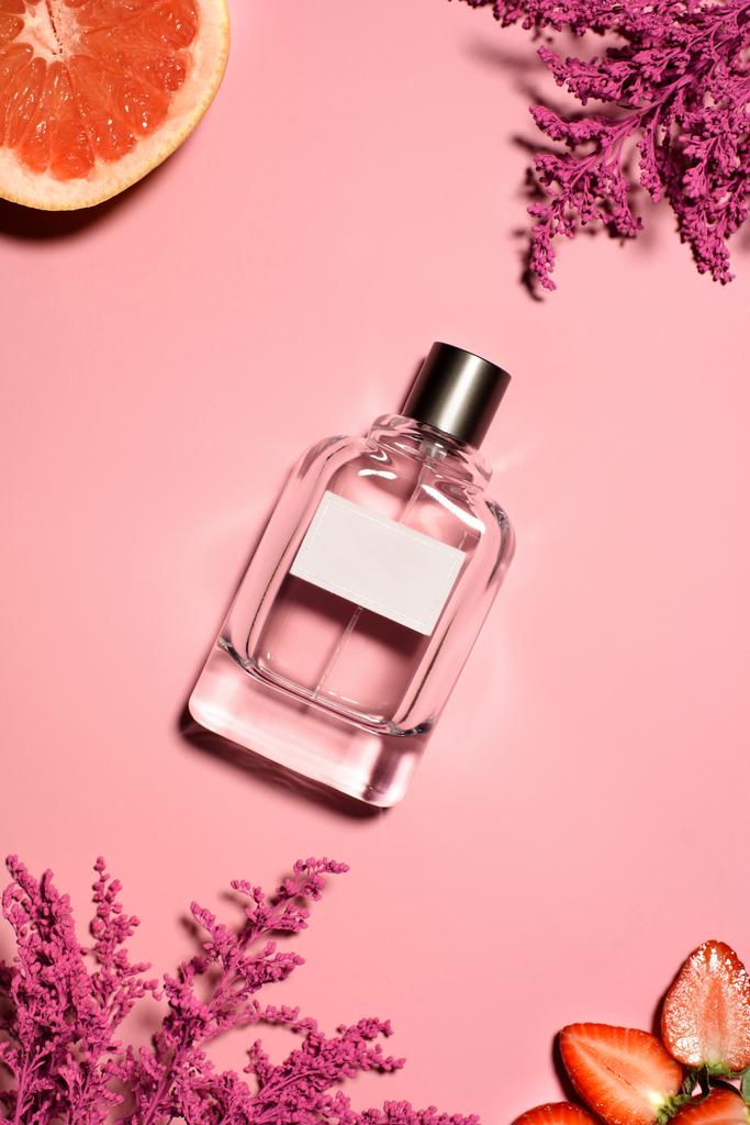 top view of bottle of perfume with pink flowers, orange and strawberry on pink surface - Photo, Image