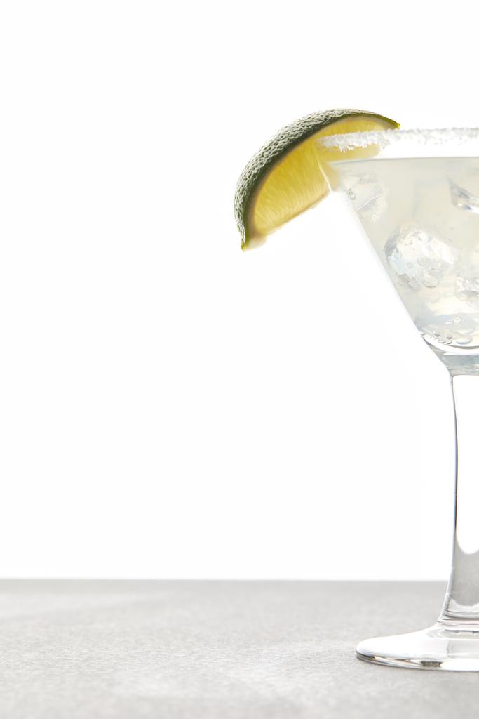 Nahaufnahme des erfrischenden Margarita-Cocktails mit Limettenstück und Eis auf Tischplatte auf weißem Hintergrund - Foto, Bild