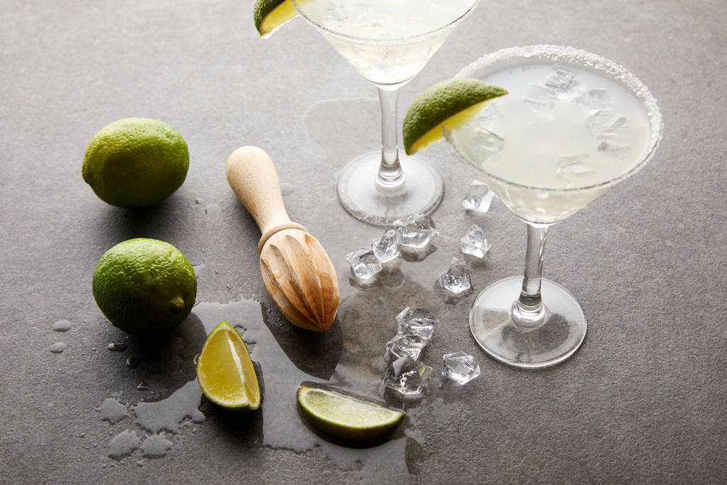 vista ravvicinata di cocktail alcolici con pezzi di lime, cubetti di ghiaccio e spremiagrumi in legno su tavolo grigio
 - Foto, immagini