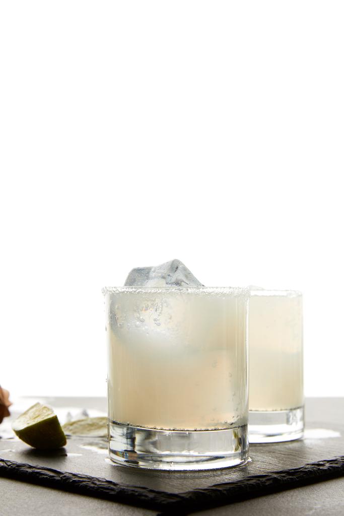 Nahaufnahme von erfrischenden Caipirinha-Cocktails mit Limette und Eis auf Tischplatte auf weißem Hintergrund - Foto, Bild