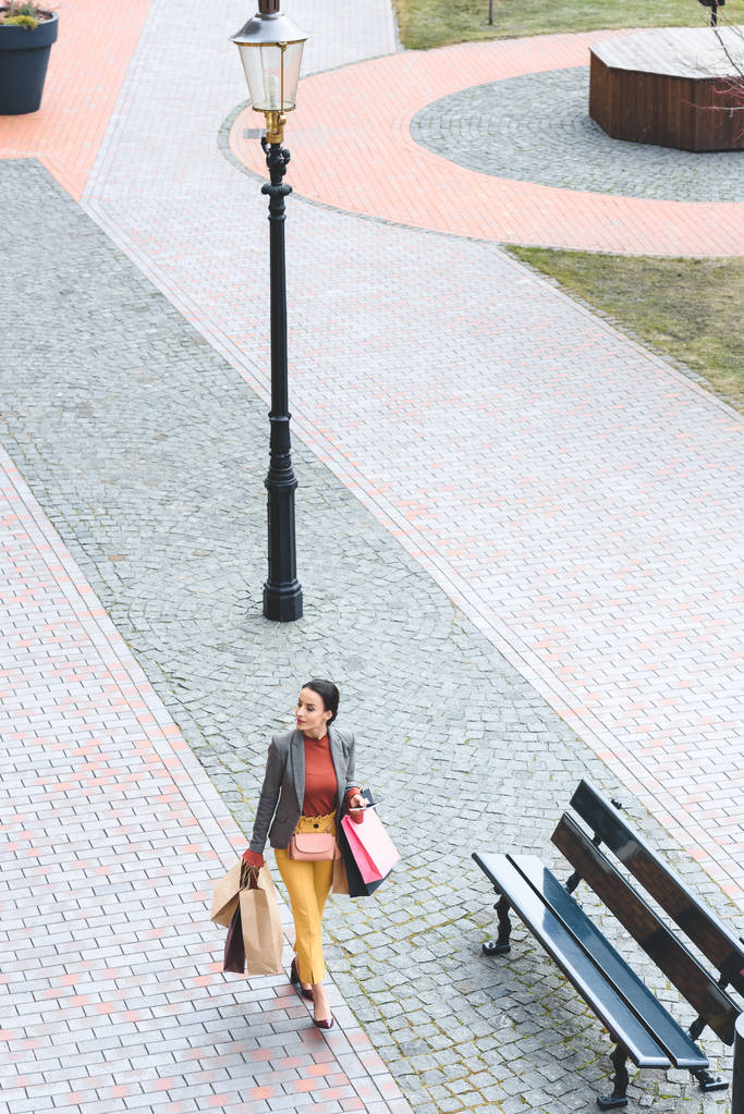 hoge hoekmening van aantrekkelijke vrouw lopen met boodschappentassen op straat - Foto, afbeelding