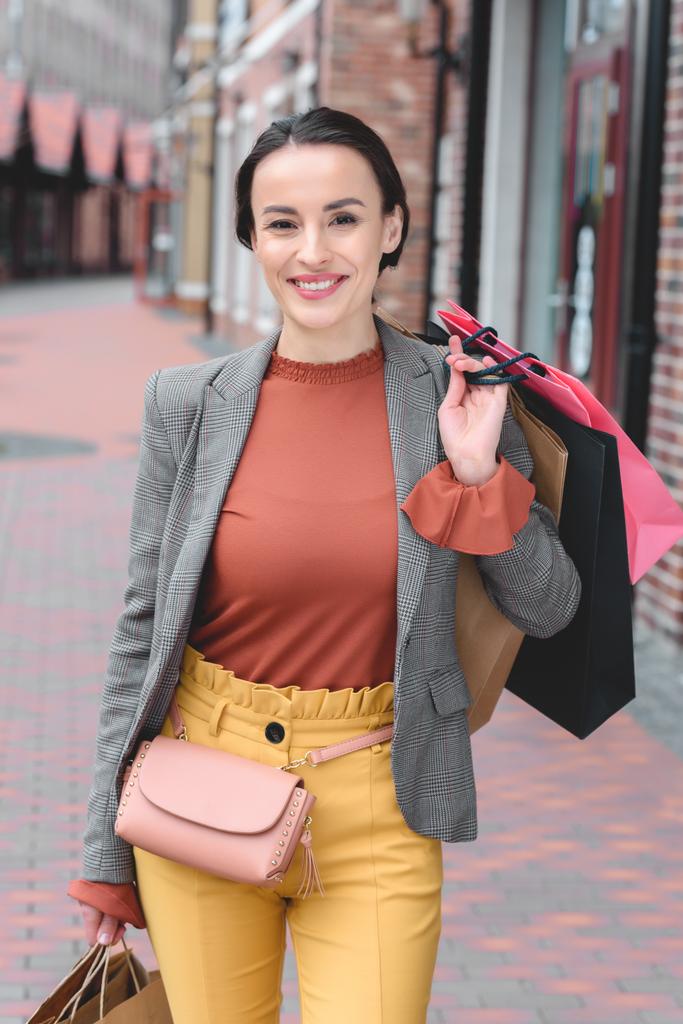 mulher atraente segurando sacos de compras no ombro e olhando para a câmera
 - Foto, Imagem