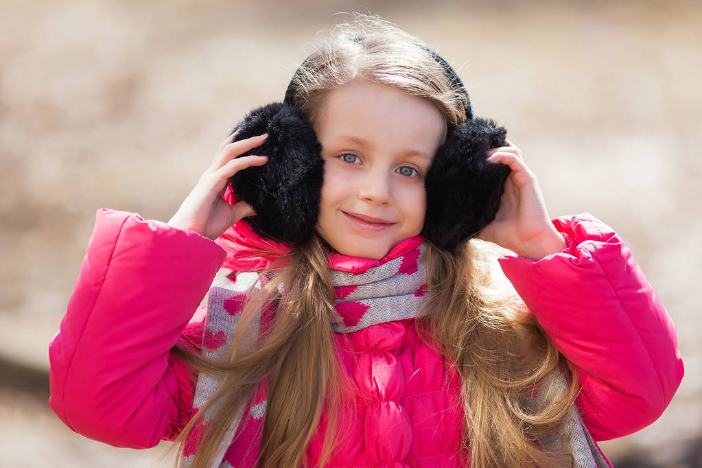 Porträt eines netten Mädchens mit Kopfhörern aus Fell an einem sonnigen Frühlingstag - Foto, Bild