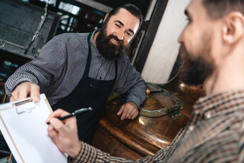 birraio barbuto in grembiule dando documenti per la firma all'uomo in camicia al birrificio
 - Foto, immagini