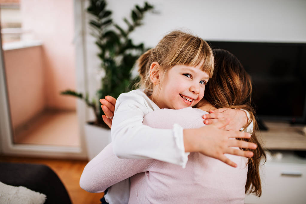 Sonriente chica rubia abrazándose con su madre en casa
. - Foto, imagen