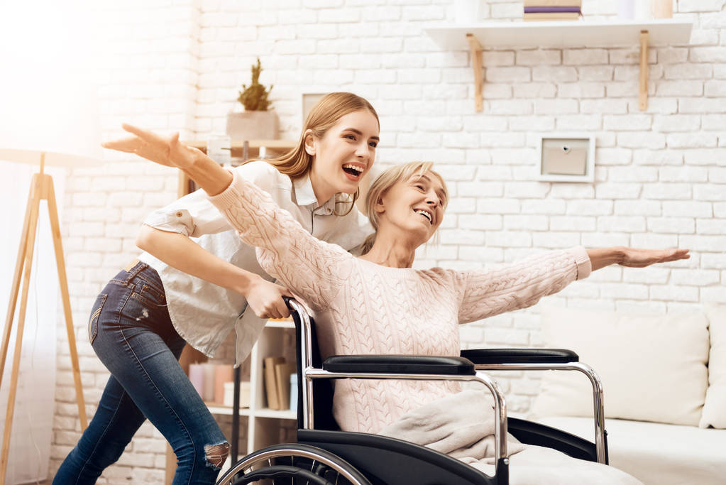 Menina amamentando mulher idosa e montando-a em cadeira de rodas
 - Foto, Imagem