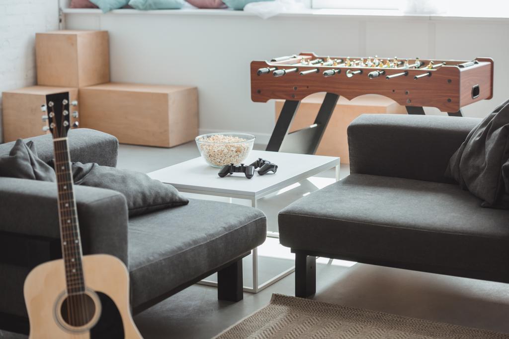 interior da moderna sala de estar com guitarra, poltronas, futebol de mesa e mesa com joysticks e pipoca
  - Foto, Imagem