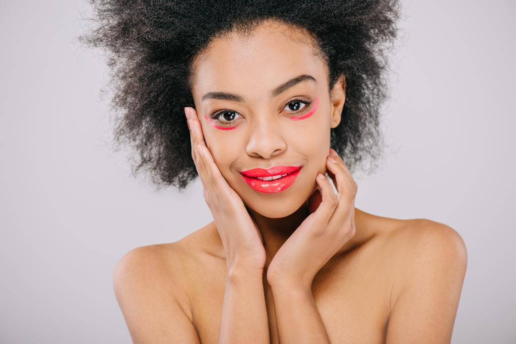 Gelukkig jonge african american vrouw met rode lippen en rode verf lijnen onder ogen geïsoleerd op grijs - Foto, afbeelding